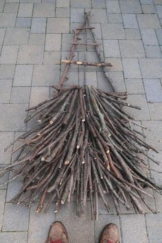 a person standing next to a pile of sticks on top of a brick sidewalk with their feet propped up