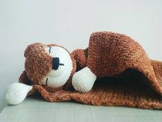 a crocheted teddy bear laying on top of a blanket with its eyes closed