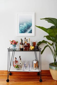 a bar cart with liquor bottles and glasses on it next to a potted plant