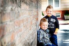 two young boys leaning against a brick wall