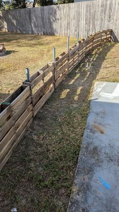 a fence made out of pallets in the yard with grass and dirt around it