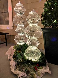 an outdoor christmas decoration with clear glass balls and evergreens on the ground next to a house