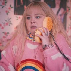 a woman talking on a phone while wearing a pink sweater with rainbow stripes and an orange ring around her neck