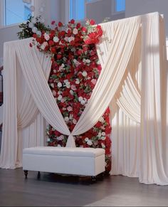 a white bench sitting in front of a flower covered wall with red and white flowers on it