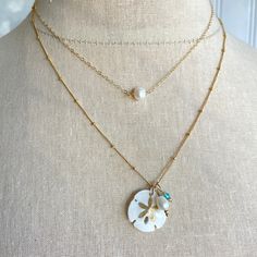 Legend has it that finding a sand dollar during a beach stroll is considered a lucky omen. So take a little bit of the beach and good luck with you wherever you go with our gorgeous Sand Dollar Charm Necklace. Features our most loved satellite chain, freshwater pearl, and blue zircon accents. Freshwater Baroque Pearl size: 6 to 8mm Blue Zircon roundel gemstone 4mm 14kt gold fill or sterling silver round beads 2mm 14kt gold fill or sterling silver satellite chain Real sand dollars are preserved a Dainty Round Jewelry For Beach, Dainty Starfish Necklace For Beach, White Delicate Chain Necklace For Beach, White Starfish Shell Necklace As A Gift, Ocean-inspired White Necklaces With Starfish Charm, White Ocean-inspired Necklaces With Starfish Charm, White Ocean-inspired Necklace With Starfish Charm, White Ocean-inspired Jewelry With Starfish Charm, Ocean-inspired White Jewelry With Starfish Charm