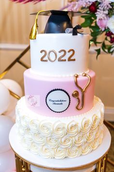 a three tiered cake decorated with white and pink icing, topped with a graduation cap