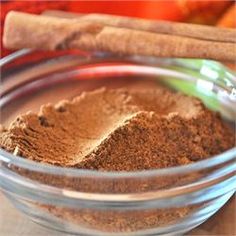 a glass bowl filled with brown powder next to cinnamon sticks