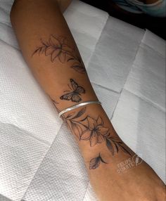 a woman's arm with flowers and butterflies tattooed on her left arm, sitting on a bed