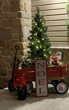 a small christmas tree sitting in a red wagon next to a sign that says noel