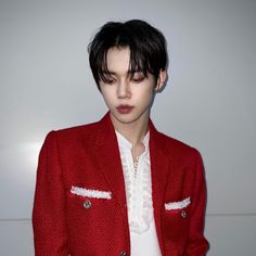 a man with black hair wearing a red jacket and white shirt, standing in front of a wall