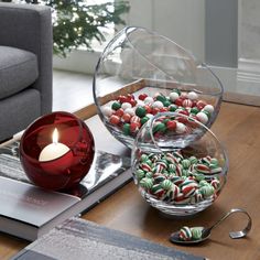 a glass bowl filled with candy next to a red candle on top of a table