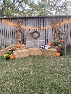 hay bales and pumpkins are arranged in front of a fence with lights on it