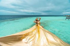 a woman in a gold dress standing on the back of a boat looking out to sea