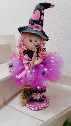 a doll dressed up as a witch holding a broom and wearing a purple tutu