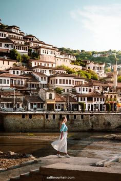 a woman standing on the edge of a body of water with buildings in the background