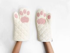 two hands wearing white gloves with pink paw prints on the front and back of them