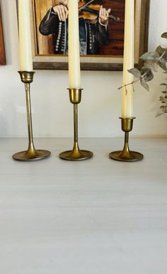 three candles sitting on top of a table next to a painting and potted plant