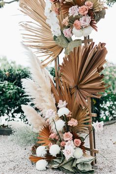 an arrangement of flowers and palm leaves is arranged on the ground in front of a tree