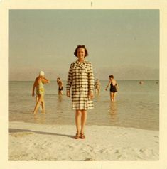 a woman standing on top of a sandy beach next to the ocean with people swimming in the water