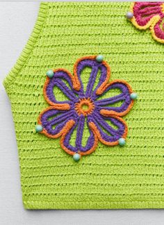 a green crocheted purse with colorful flowers on the front and side, sitting on a white surface