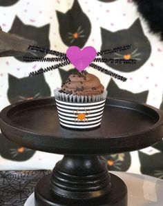 a cupcake sitting on top of a cake plate with a spider decoration above it