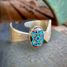 This vintage bracelet features a stamped sterling silver shank that is contemporary in style with a zig-zag-ish form atop which sits an oval bezel with intricate inlay pattern. The piece was made by Roderick and Marilyn Tenorio for Carolyn Pollack's Relios, an Albuquerque based company that employed Native American artists. From a gallery representing Tenorios: "Roderick Tenorio and his wife, Marilyn, often collaborate on making jewelry and each also works separately.  Roderick graduated from Albuquerque High School in 1981, then attended the Institute of American Indian Arts in Santa Fe. He served time in the U. S. Army. He is a top prizewinning artist from Santo Domingo Pueblo. Marilyn Tenorio is a Navajo and works in mosaic inlay as well as silver and gold jewelry." Examine the oval-sha Adjustable Turquoise Inlay Bracelets, Adjustable Turquoise Bracelet With Inlay, Artisan Turquoise Engraved Bracelets, Artisan Turquoise Engraved Bracelet, Southwestern Turquoise Etched Jewelry, Southwestern Etched Turquoise Jewelry, Southwestern Style Etched Turquoise Jewelry, Southwestern Inlay Cuff Bracelet Gift, Adjustable Turquoise Sterling Silver Artisan Bracelet