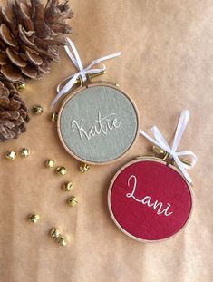 two personalized christmas ornament hanging on a table next to pineconis