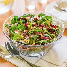 a glass bowl filled with salad on top of a wooden table next to silverware