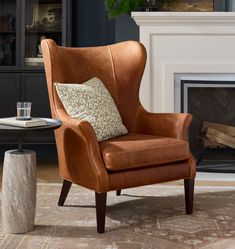 a brown leather chair sitting in front of a fireplace with a pillow on it's back