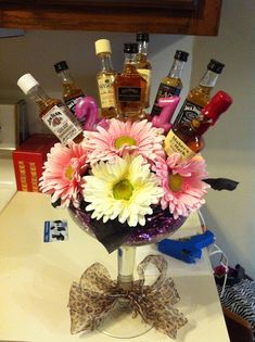 a glass vase filled with lots of different types of liquor and flowers on top of a counter