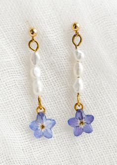 two blue and white flowers are hanging from gold - plated earwires on a white cloth