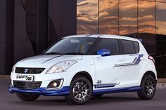 a white suzuki swift car parked in front of a building with windows and sunset behind it