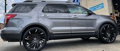 the back end of a silver suv parked in front of a building with black rims