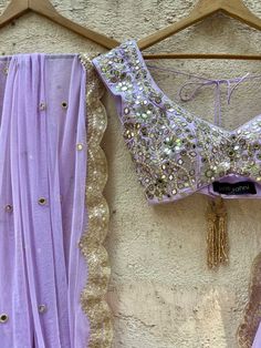 A three-piece lavender lucknowi mirror lehenga set from the Priti Sahni collection. This elegant lavender georgette lehenga with heavy gota, sequins, pearl and zari work border is paired with lavender blouse in raw silk fabric with mirror, pearl and zardozi hand work embroidery. The lehenga has side hanging ball tassels to the waistline. And the blouse has a sequins tassel tie-up at the back. The outfit is completed with a lavender mirror net dupatta with scalloped edging. Mirror Lehenga, Haldi Outfit, Mirror Work Blouse, Georgette Lehenga, Lavender Blouse, Raw Silk Fabric, Hand Work Embroidery, Zari Work, Net Dupatta