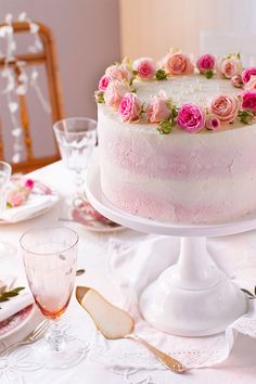 a white cake with pink flowers on it sitting on a table next to glasses and plates