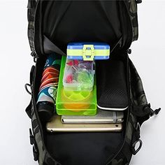 an open backpack filled with various items on top of a white table next to a cell phone