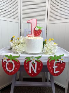 a one year old birthday cake with flowers and strawberries on the table next to it