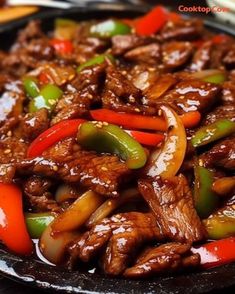 beef and peppers in sauce on a black plate