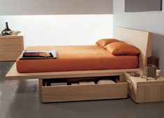 a bed with an orange blanket and some drawers underneath it in a room that has white walls