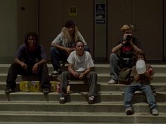 four people sitting on steps with skateboards and one person holding a camera in front of them