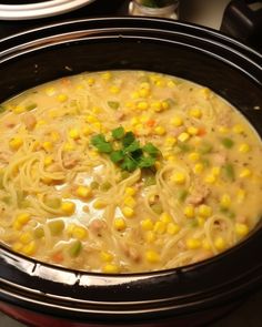 a bowl of chicken noodle soup with corn and parsley on the top, ready to be eaten