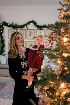 a woman holding a baby next to a christmas tree