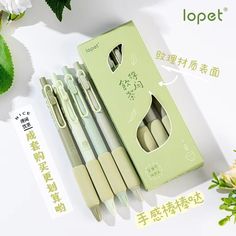 four pens are sitting in a green box next to some flowers and paper with chinese writing on it