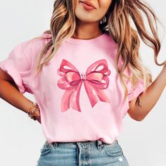 Embrace elegance and flirtatious charm with our captivating pink bow shirt, a delightful addition to your coquette-inspired wardrobe! 🌸👚 This shirt embodies the essence of femininity and playfulness, perfect for those who adore a touch of chic sophistication with a hint of flirtation. 🌷 The darling pink hue complements the shirt's design, accentuating the focal point--an exquisitely crafted oversized bow adorning the neckline or sleeves, adding a whimsical and flirtatious allure to your ensem Feminine Pink Crew Neck T-shirt, Feminine Party Tops With Bow Detail, Feminine Pink Summer Shirt, Pink Party Top With Bow, Feminine Pink Shirt For Summer, Pink Tops With Bow For Party, Spring Party Tops With Ribbon, Trendy Pink Party Shirt, Cute Bow T-shirt For Spring