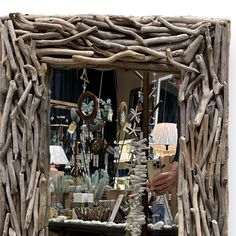 a man is holding up a mirror made out of driftwood sticks and other items