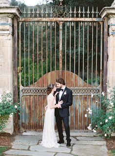 a bride and groom standing in front of an iron gate