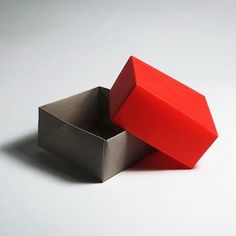 a red box sitting on top of a white table next to a silver container filled with something