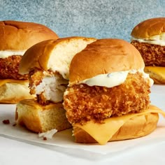 three fried chicken sandwiches with cheese and mayonnaise sitting on top of each other