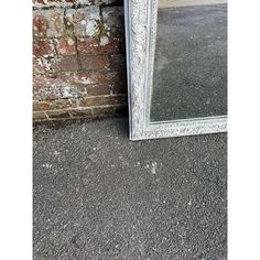 a large white mirror sitting on the ground next to a brick wall and cement floor