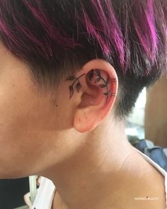 a woman with pink hair has a small tattoo on her left side behind the ear